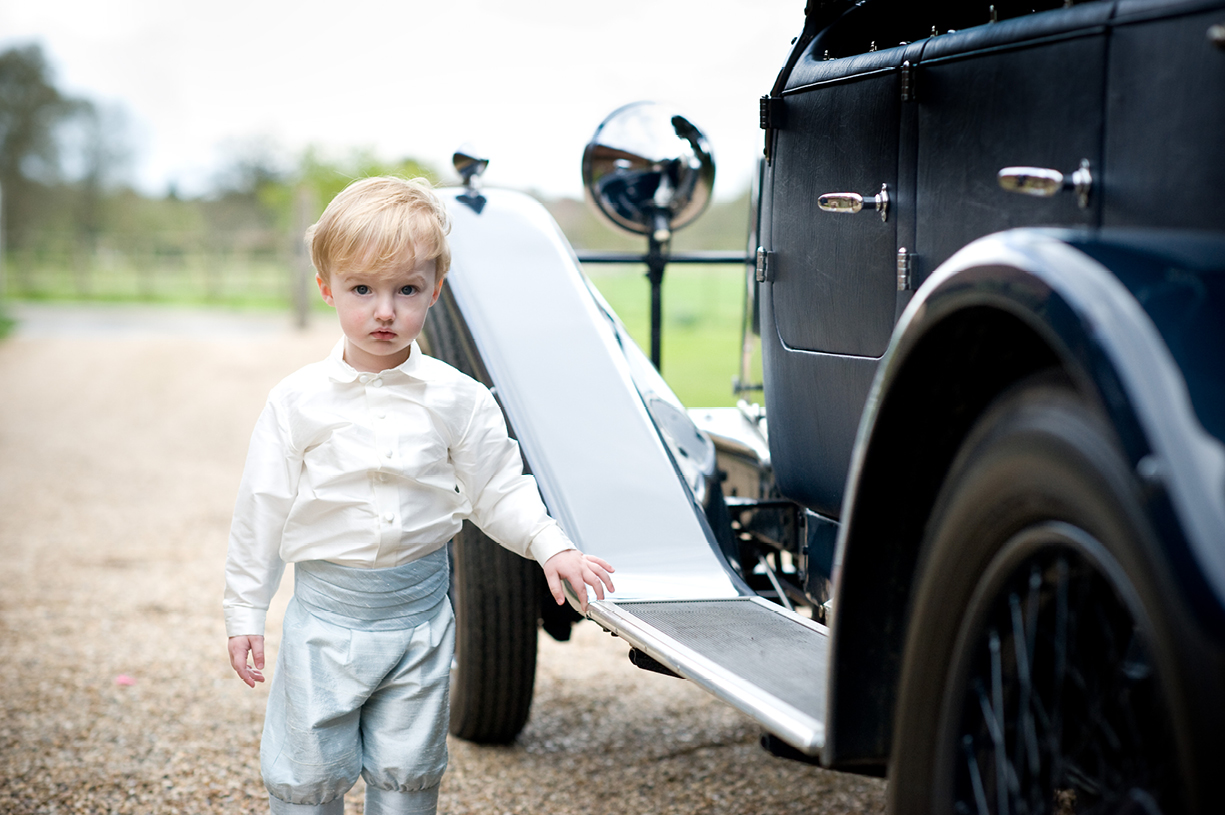 portrait photo of young pageboy admiring Rolls Royce while waiting for bride at summer wedding 